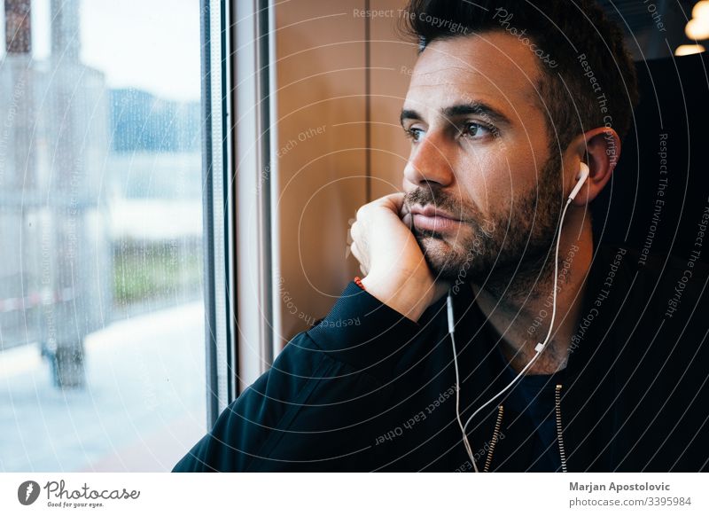 Young man traveling by train wearing earphones 30s adult alone bearded casual caucasian commute commuter day everyday guy handsome headphones journey life