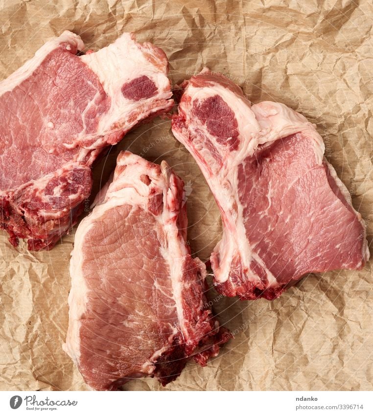 raw juicy pork slices of meat on the rib, food lies on brown parchment paper barbecue bbq black board bone chop cook cooking cuisine cut dark dinner fat fillet