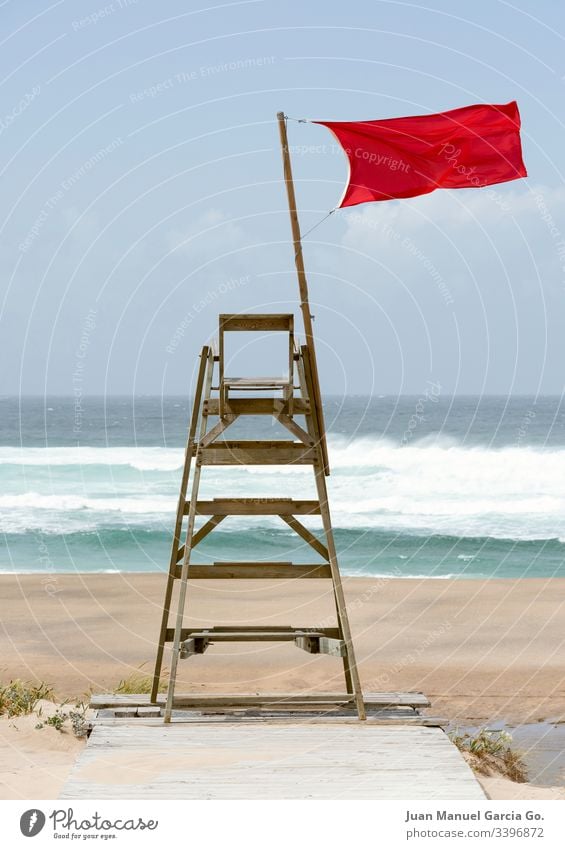 Lifeguard chair sitting empty with a red flag streaming in the wind a coruña aquatic beach blue coast danger drown isolated life lifeguard no people nobody