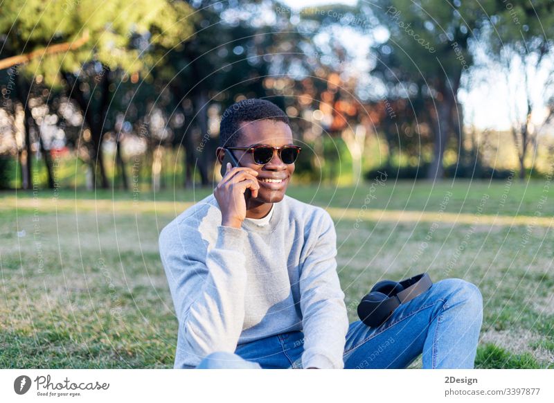 Fashionable black male with sunglasses sitting outdoors checking his news feed or messaging via social networks using cell phone outside lifestyle american