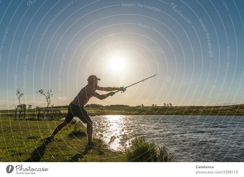 Young man casts a fishing rod on the lake shore, the sun is shining, the water is shining Fishing (Angle) Fisherman Fishing rod Colour photo coast Food Lake