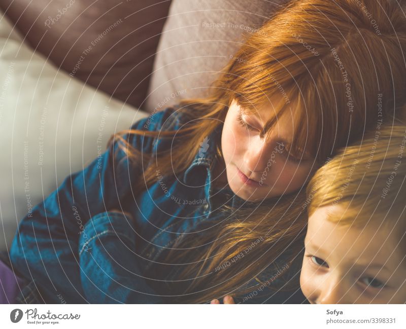 Two blonde little kids in blue on gray sofa child smile face family siblings brother sister redhead funny sweet tender together indoors portrait people shirt