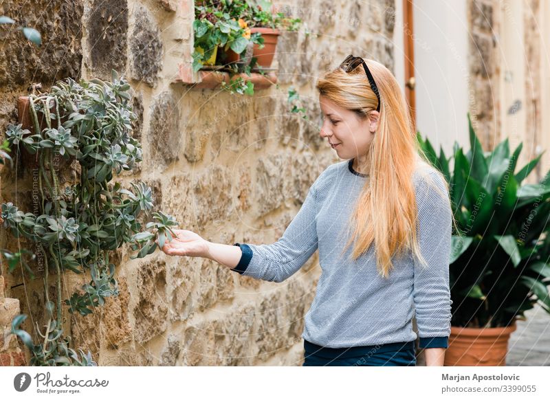 Young female traveler in the streets of an old town in Tuscany, Italy admiring floral decorations on the building alley ancient casual caucasian city enjoying