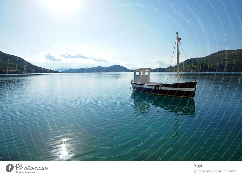 Dark Blue Fishing Boat Anchored in a Bay aegean blue boat calm clouds dark blue island hills meditearranean ocean old peaceful reflection sea shining sky sun