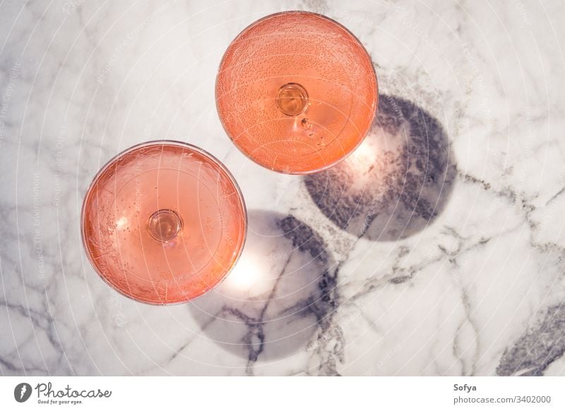 Two crystal stemmed glasses with rose wine outdoors on marble table in hard light producing shadows white party pink drink dinner luxury background modern