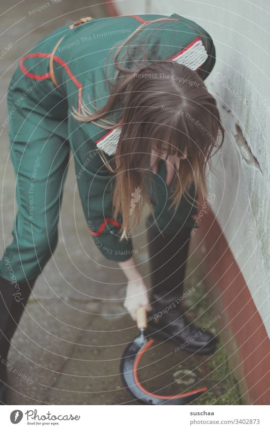 girl in uniform tries to remove weeds with a sickle Girl Young woman Uniform Tool Weapon Youth (Young adults) Socialism Caretaker Courtyard Wall (barrier)