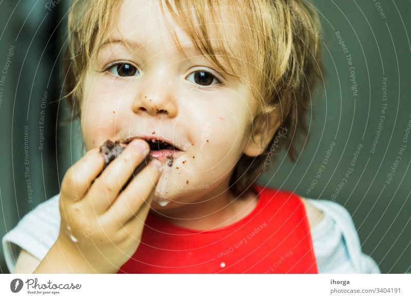 portrait adorable child eating chocolate sponge cake attribute baby background bib boy brown candy childhood cute delicious desert dessert dirty fat flavour