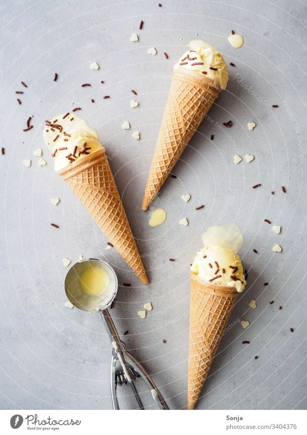 Vanilleeis in Eistüten mit Streusel, Herzen und einen Portionierer auf einem grauen Hintergrund, Flat lay vanilleeis kugel eistüte waffel eisportionierer