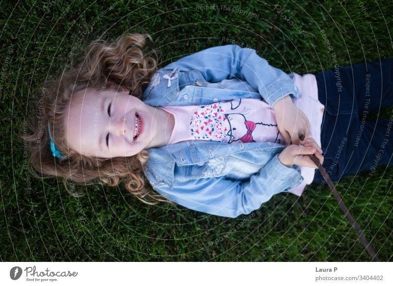 Beautiful blonde little girl laying on the grass, laughing - seen from above beautiful portrait child kid back green summer playing stick joy nature family time