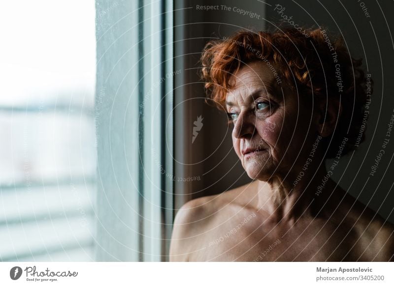 Mature woman by the window thinking about life adult age aged aging alone beautiful beauty care caucasian close-up closeup contemplating depression elder