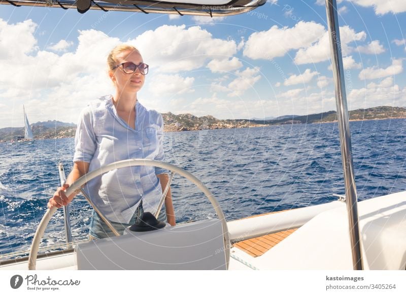 Attractive blond female skipper navigating the fancy catamaran sailboat on sunny summer day on calm blue sea water. nautical steering wheel sailing boat woman