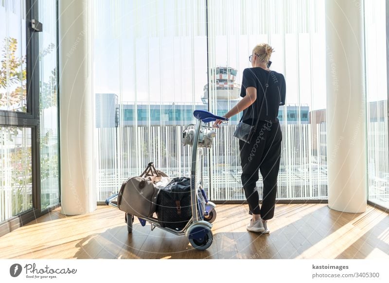 Casual woman on airport terminal talking on the cell phone, waiting for flight departure with luggage on trolley cart. travel international passenger tourist