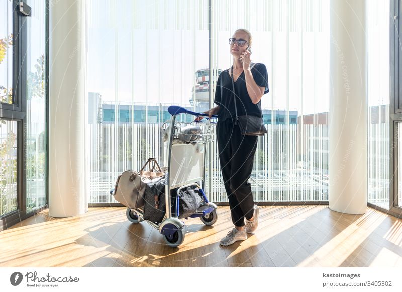 Casual woman on airport terminal talking on the cell phone, waiting for flight departure with luggage on trolley cart. travel international passenger tourist