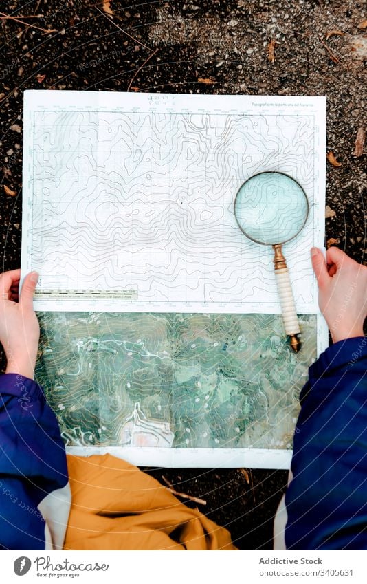 Unrecognizable hiker navigating with map and compass in countryside navigate traveler check topographic map magnifying glass ground equipment cartography tool