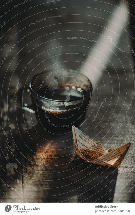 Small paper boat near coffee cup retro table shabby hot decor sunlight ray beam weathered ancient grunge timber lumber brew art creative page small tiny