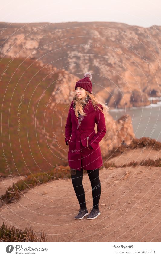 Young woman on a red coat contemplating the sea from the top of a cliff one standing atlantic water scenic landmark edge marin light space Sintra safety beauty