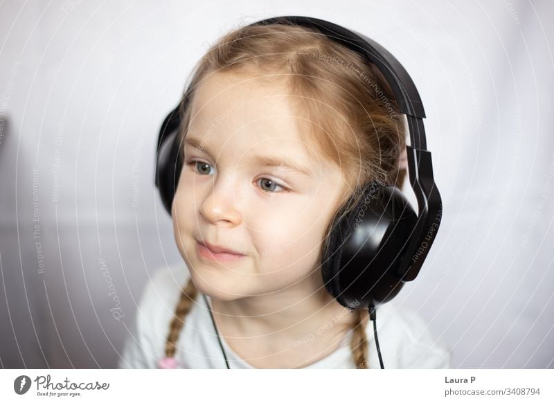 Close up of a beautiful blonde little girl listening to music at headphones smile happy young beauty child kid daughter fun cute enjoy isolated person