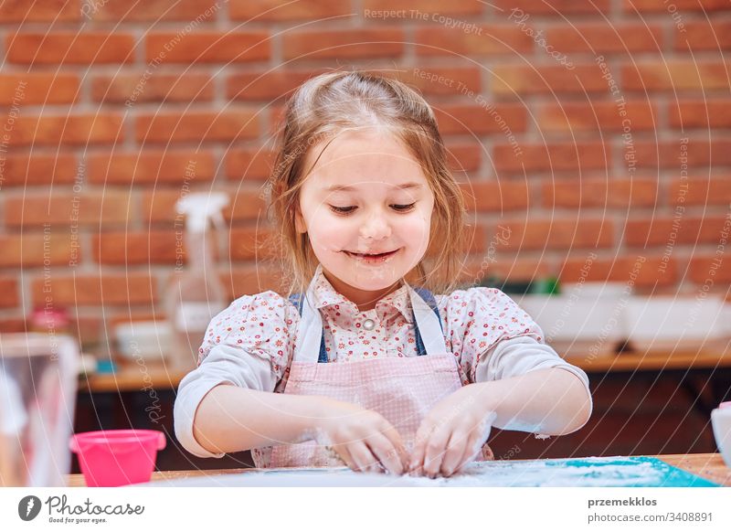 Little girl eating the icing sugar left after baking cookies. Kid taking part in baking workshop. Baking classes for children, aspiring little chefs. Learning to cook. Combining and stirring prepared ingredients. Real people, authentic situations