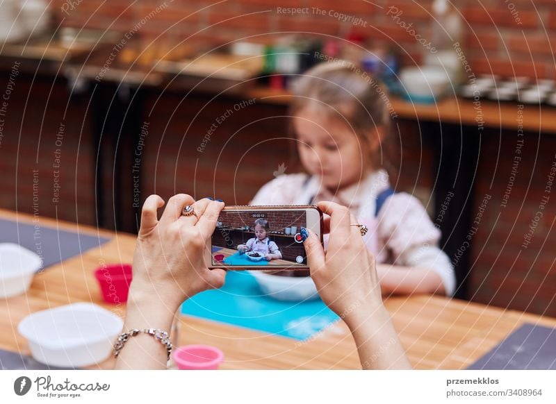 Mom recording her little daughter while taking part in baking workshop. Baking classes for children, aspiring little chefs. Learning to cook. Combining and stirring prepared ingredients. Real people, authentic situations