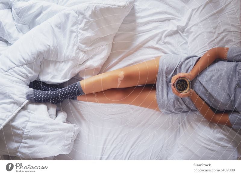 Young woman enjoying her coffee while sitting in bed. cozy morning cup girl home book legs soft socks top view young warm bedroom beautiful white hands comfort