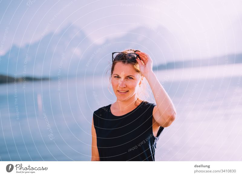 young woman in backlight at a lake with mountains in the background Contentment tranquillity relaxed Serene Joy Person wearing glasses Relaxation Laughter