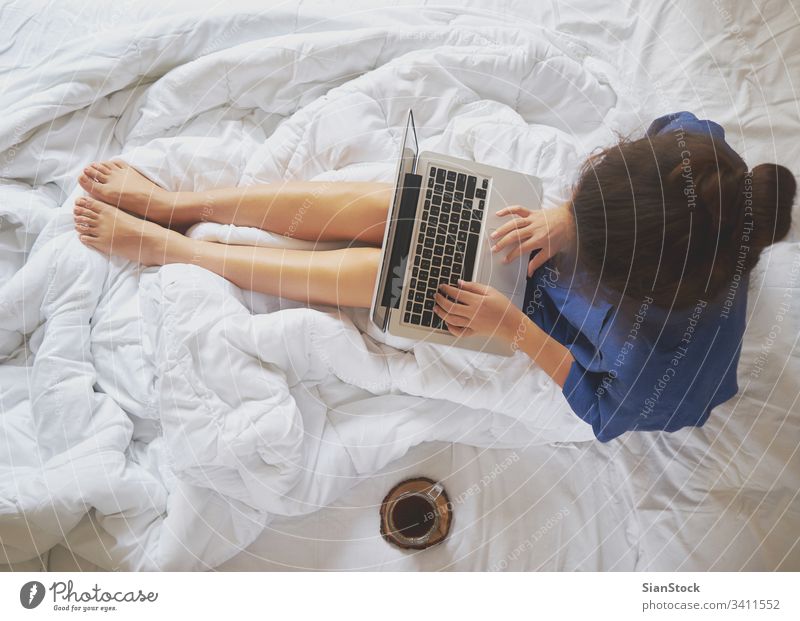 Young woman drinking coffee at home in her bed and checking her laptop cozy morning cup girl book legs soft view young warm bedroom beautiful white hands