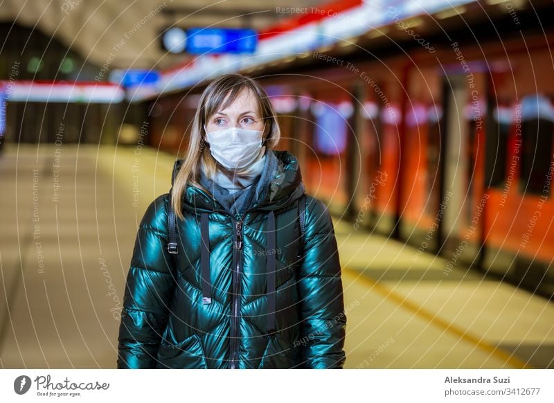 Woman in winter coat with protective mask on face standing on metro station, waiting for train, looking worried. Preventive measures in public places of epidemic regions. Finland, Espoo