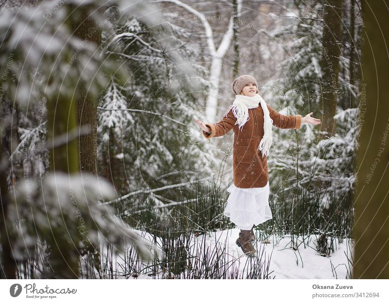 A 7 year old girl in a brown sheepskin coat walks in the forest. Concept of the seasons, a winter fairy tale. Snow, trees. baby background beautiful beauty blue