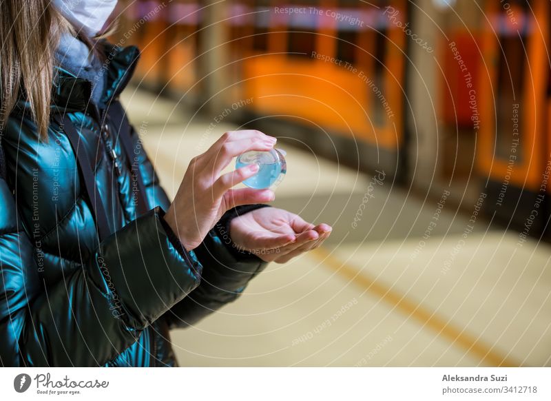 Woman in winter coat with protective mask on face standing on metro station, using hand sanitizer, looking worried. Preventive measures in public places of epidemic regions. Finland, Espoo