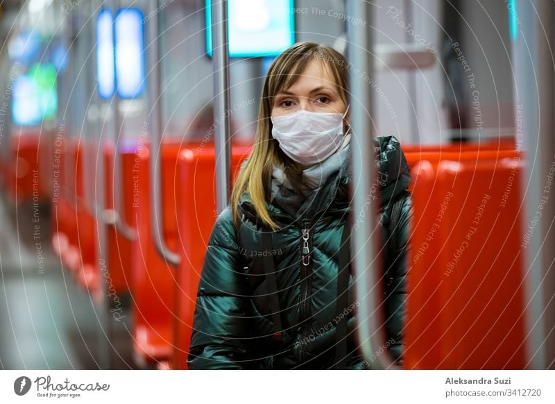 Woman in winter coat with protective mask on face standing in subway car, using phone, looking worried. Preventive measures in public places of epidemic regions. Finland, Espoo