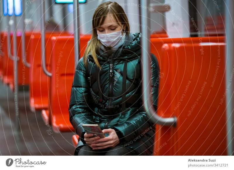 Woman in winter coat with protective mask on face standing in subway car, using phone, looking worried. Preventive measures in public places of epidemic regions. Finland, Espoo