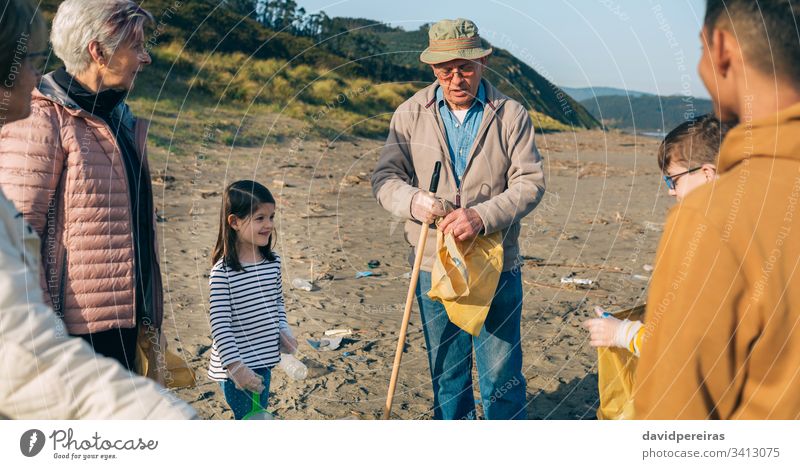 Volunteers preparing to clean the beach senior volunteer explaining organizing garbage bags family group rake granddaughter hat tools man environment child