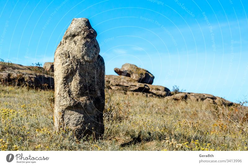 ancient stone idol in a field amidst stones grass historical history monument nature old pagan idol paganism sky statue tradition wildflowers