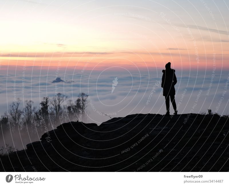 Lone female hiker contemplating the clouds from the top of a mountain lone alone beanie hat above hiking tourist tourism landscape altitude silhouette sunset