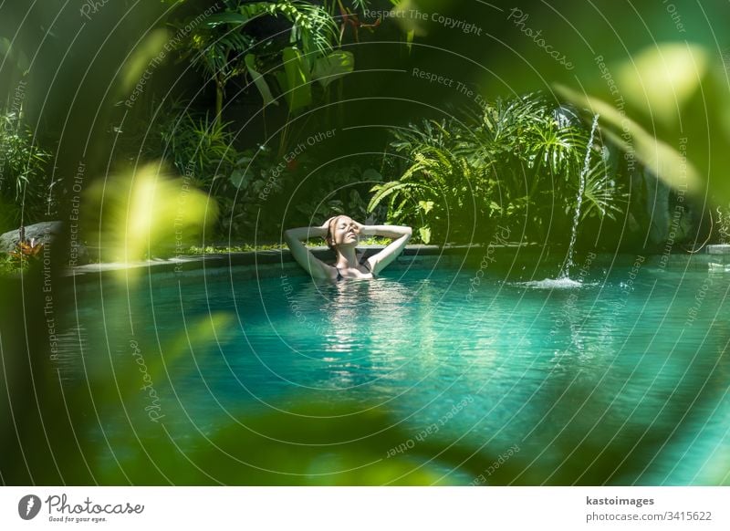 Sensual young woman relaxing in outdoor spa infinity swimming pool surrounded with lush tropical greenery of Ubud, Bali. wellness water nature beauty beautiful