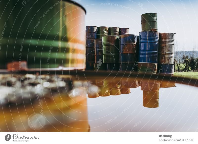 Stacked up, rusty metal barrels are reflected in puddle Threat Environmental damage Part Dry Background picture Environmental protection Damage