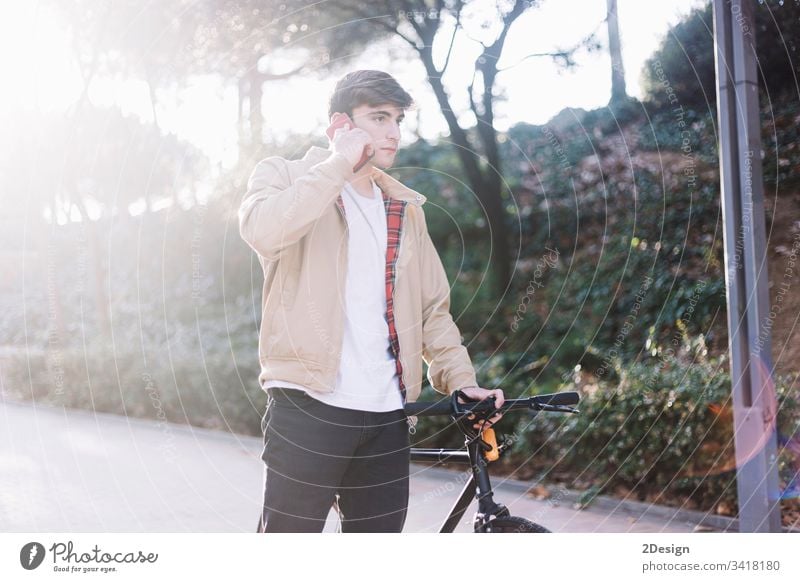 Young hispanic man using mobile and carrying a bike while walking outdoors holding young 1 happy face person male cool calling casual attire phone adult bench