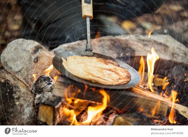 Man and woman making pancakes on campfire in forest on shore of lake, making a fire, grilling. Happy couple exploring Finland. Scandinavian landscape. active