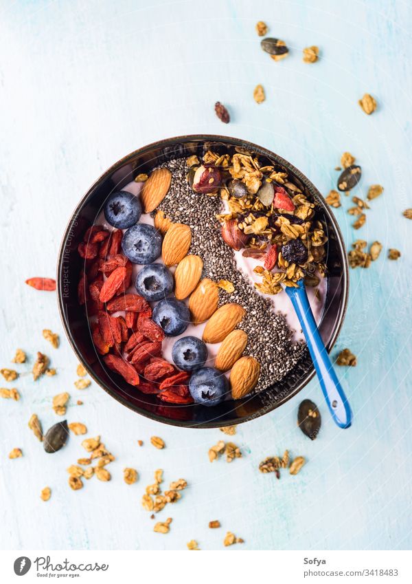 Yogurt smoothie bowl with berries, chia, granola yogurt nuts chia seeds almond goji raspberry colorful pastel turquoise matcha tea wooden background blueberry