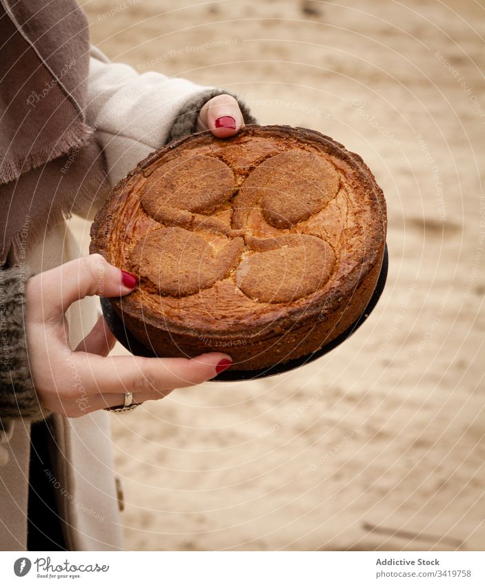 Anonymous woman holding pie on beach picnic sea sky cloudy weekend coat female style trendy coast holiday lifestyle shore elegant fresh food season tasty