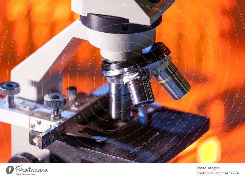 Close up of microscope lenses focused on a specimen in warm orange light light. research science experiment technology biology biotechnology education discovery