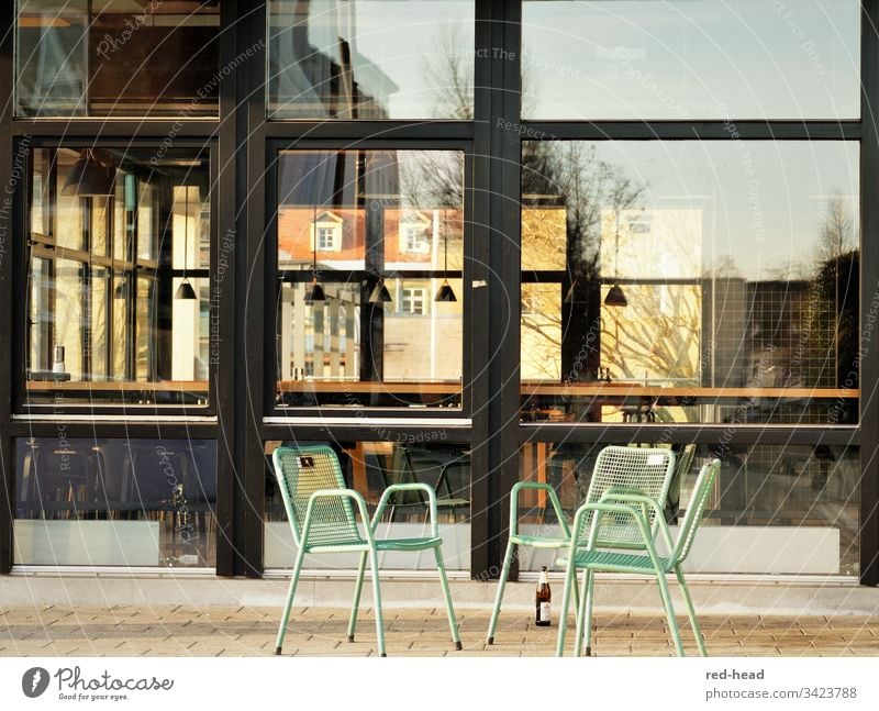 deserted chairs on a public square in front of an empty canteen - with a single beer bottle left standing - Group of chairs Glas facade Gloomy Chair Steel