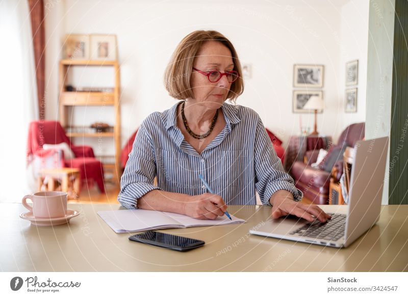 Middle age senior woman working at home using computer female laptop mature people one house person lifestyle desk drink glasses attractive relax technology job