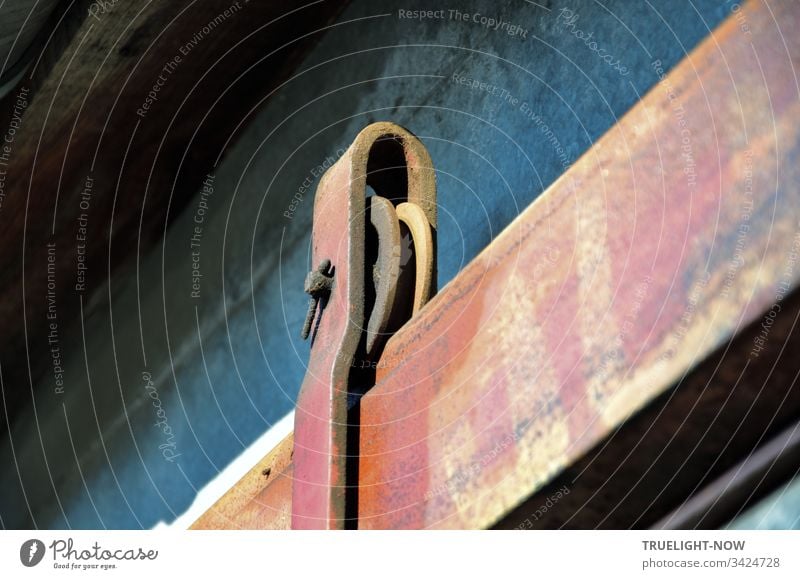 Detail of an old, heavy, U-shaped iron construction holding an iron wheel that rolls in one axis on a rail, allowing the movement of a sliding gate suspended from it in the horizontal plane.