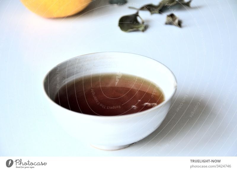 Freshly brewed Asssam tea in a light Chinese ceramic bowl on a white table with some fallen leaves and a grapefruit- Tea Black tea tea bowl Drinking White Brown