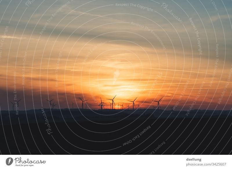 Sunset over a field with wind turbines Clouds Sky Field Pinwheel windmills Power Generation Energy Infrastructure Wind energy plant Colour photo Energy industry