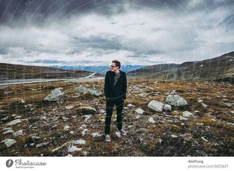 A young man is standing alone in the landscape, but the sky is cloudy. Anyway. Full-length on one's own Freedom Laughter Positive Moody Life Nature Adults