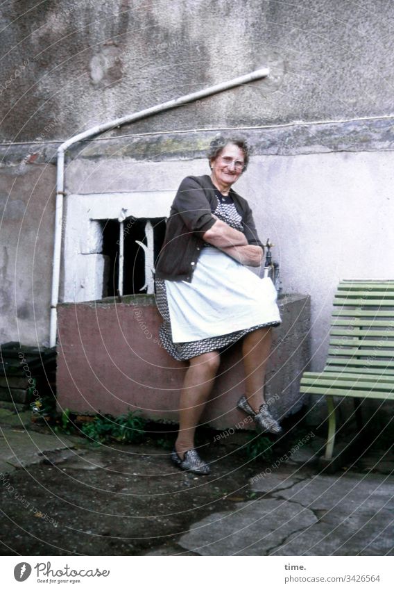 Power & goodness Woman Senior citizen Backyard Apron Sit Bench Drainpipe Concrete Wall (building) Wall (barrier) dwell Window kind Cardigan Smiling Dress