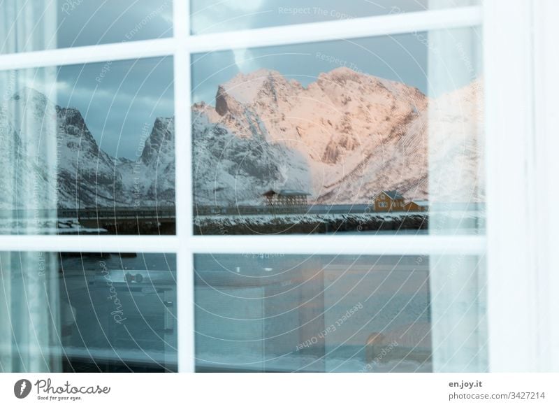 Small yellow house on the fjord in front of snow-covered mountains is reflected in the window pane North Relaxation Winter vacation Snow Central perspective