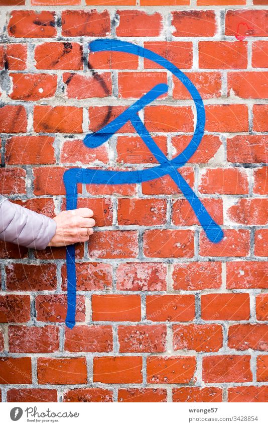 A woman's hand apparently holds a hammer and a sickle - graffito in front of a red brick wall Graffiti Graffito Hand Women`s hand hammer and sickle Brick wall